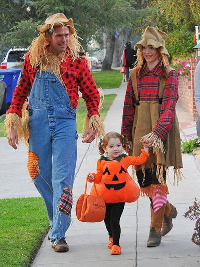 two people in costumes walking down the sidewalk with a child dressed as a scarecrow