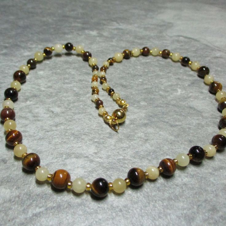 This necklace is made from Tigers Eye gemstone beads, in three sizes, alternate with 2 sizes of yellow Jasper separated by gold coloured glass seed beads. The Tigers Eye gemstones are 4mm at each end of the necklace changing to 6mm then 8mm at the centre, while the Jasper is 4mm at each end changing to 6mm. The magnetic clasp is gold plated stainless steel and the necklace comes with free matching earrings all enclosed within a cream fine velvet bag. Yellow Spiritual Beaded Necklace With Gemstone Beads, Gold Natural Stones Round Beads, Gold Round Beads With Natural Stones, Amber Beaded Necklaces With Spacer Beads As Gift, Gold Spiritual Gemstone Beads, Gold Necklaces With Round Natural Stones, Gold Necklace With Round Natural Stone Beads, Gold Necklace With Round Natural Stones, Spiritual Gold Beads Gems And Cabochons With Natural Stones