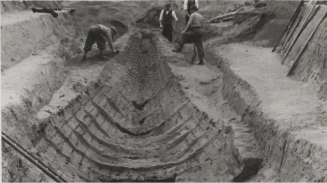 some people digging in the dirt with two men standing next to them and another man looking on