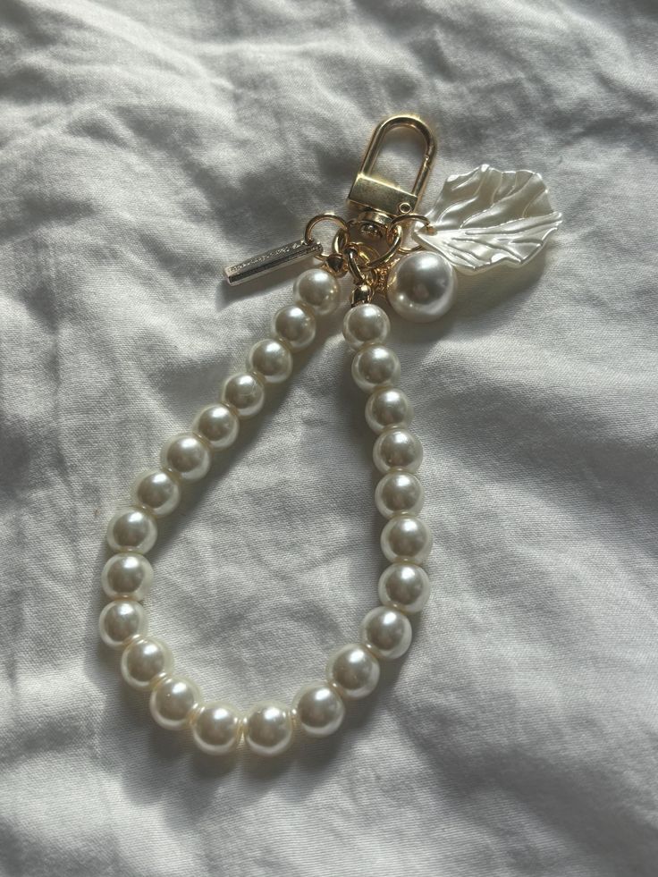 a white beaded bracelet with a leaf charm hanging from it's end on a bed