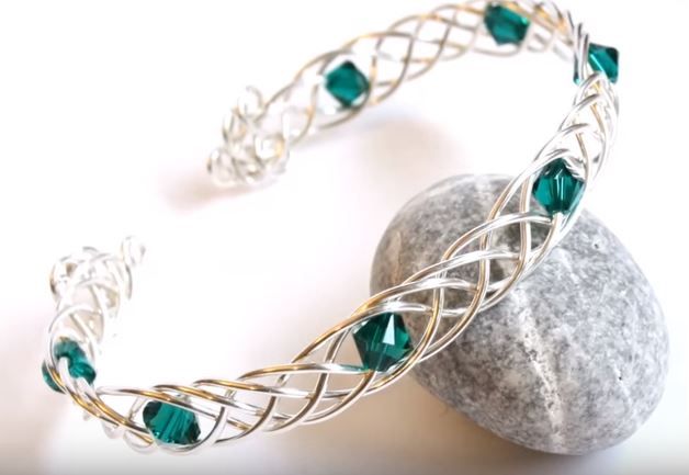 a silver and green bracelet sitting on top of a rock