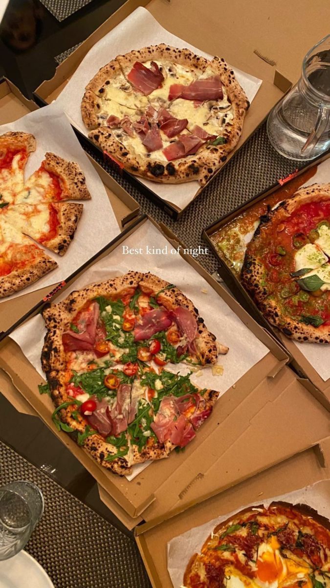 four different types of pizzas in boxes on a table with glasses and water bottles