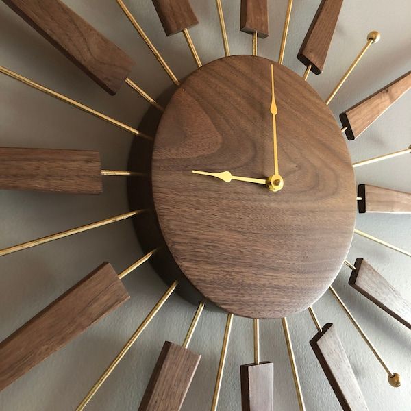 a clock made out of wood and gold sticks on the face is shown in front of a white wall