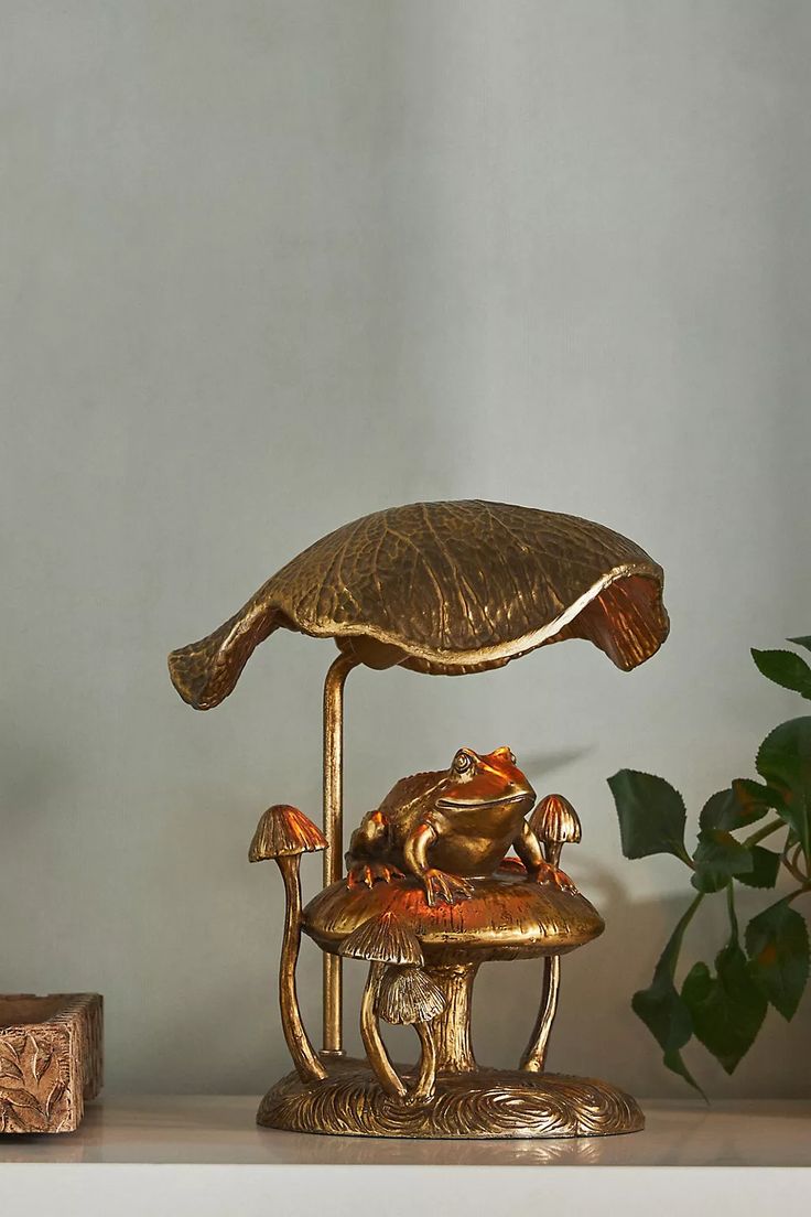 a gold frog lamp sitting on top of a table next to a potted plant