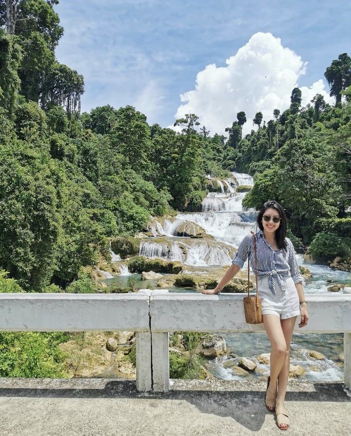 a woman standing on a bridge next to a waterfall