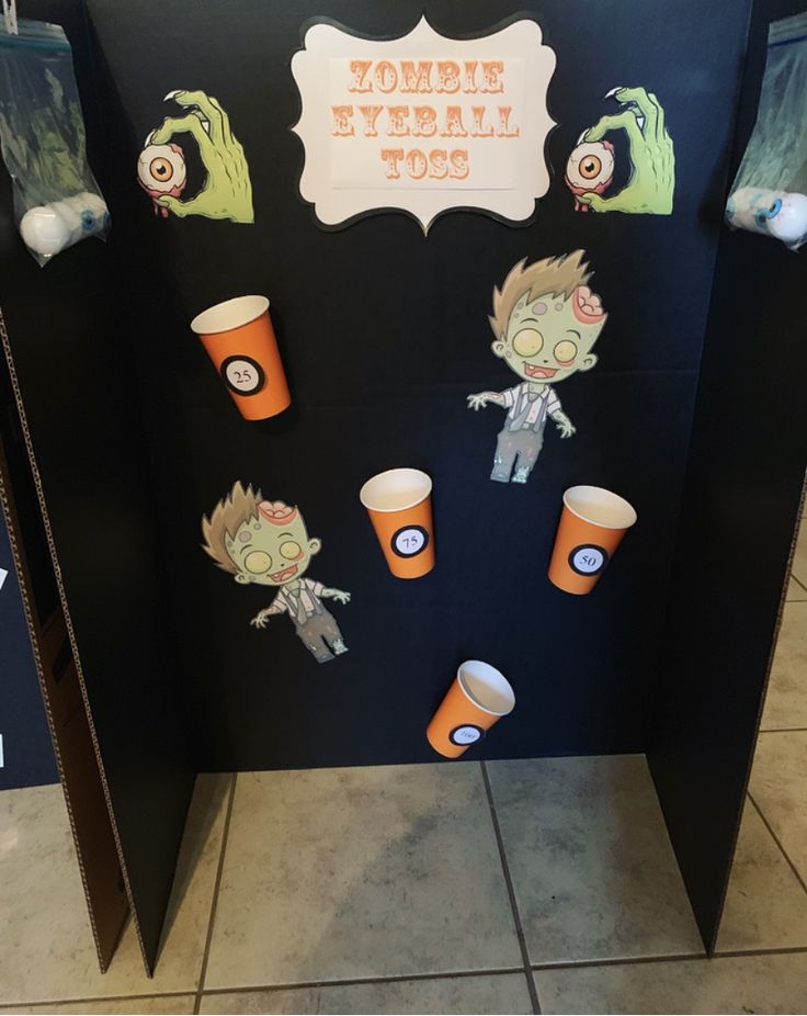 a bathroom stall decorated with paper cups and zombie faces on it's sides, in front of a sign that says zombie tybal toes