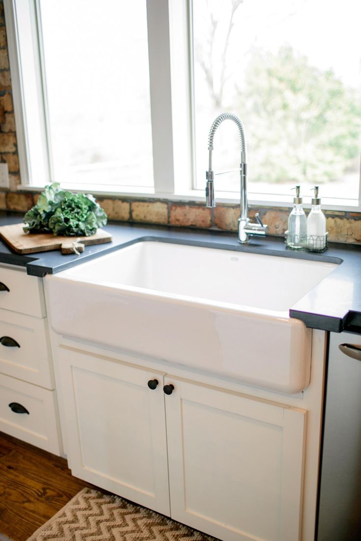 a white kitchen sink sitting under a window next to a counter top with a cutting board on it