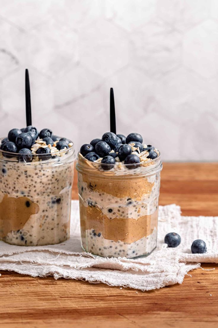 two jars filled with blueberries and oatmeal on top of a wooden table