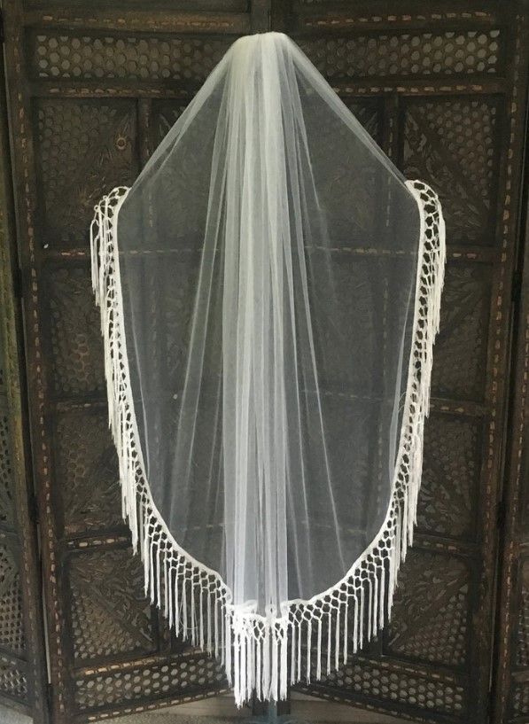 a white veil hanging from the side of a wooden door with fringes on it