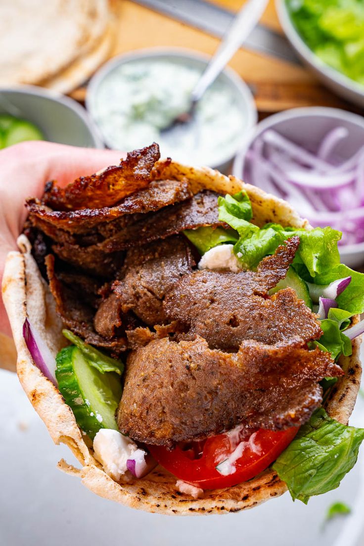 a hand holding a sandwich with meat, lettuce and tomato on it in front of some other food