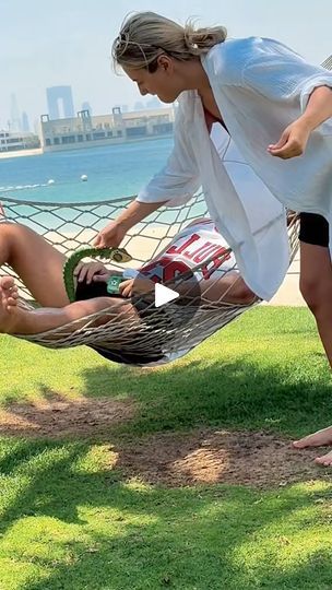 two women sitting in a hammock on the grass by the ocean with their feet propped up