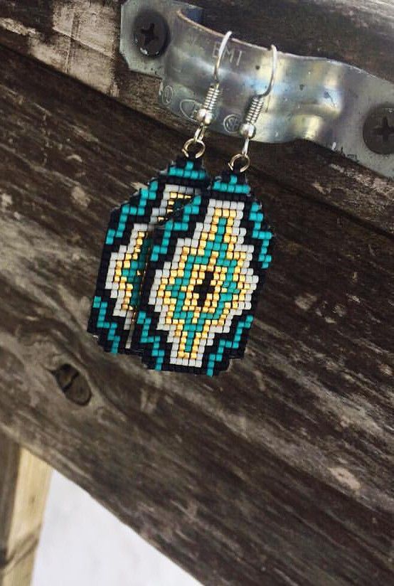 a pair of beaded earrings hanging from a wooden table next to metal hooks