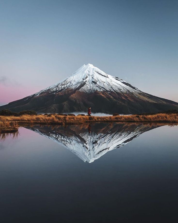 a person standing in front of a lake with a mountain in the background at sunset