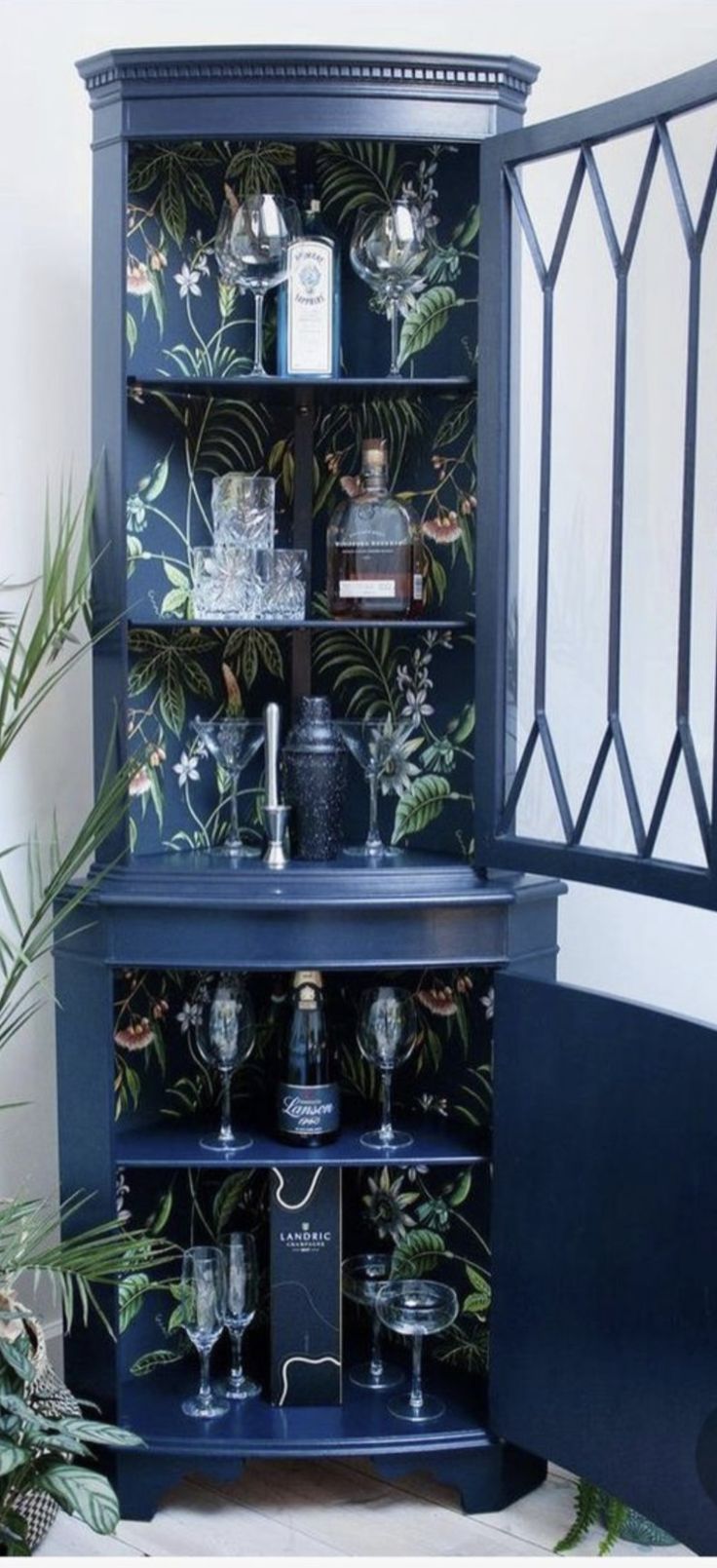 a blue cabinet with wine glasses and liquor bottles in it next to a potted plant