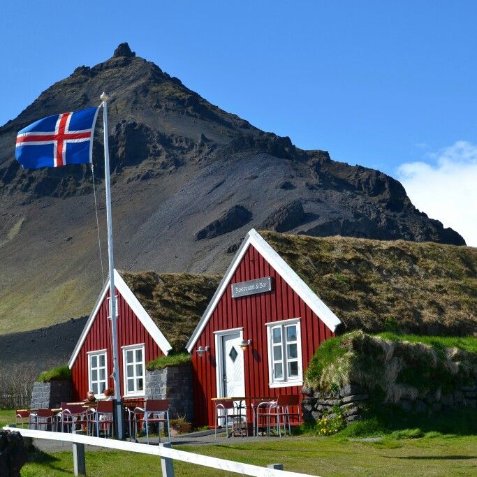 a red house with a flag on the roof and mountains in the backgroud