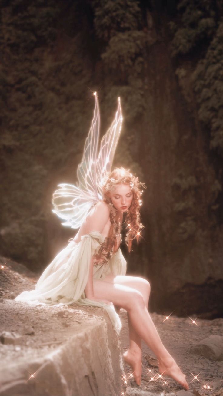 a woman dressed as a fairy sitting on a rock