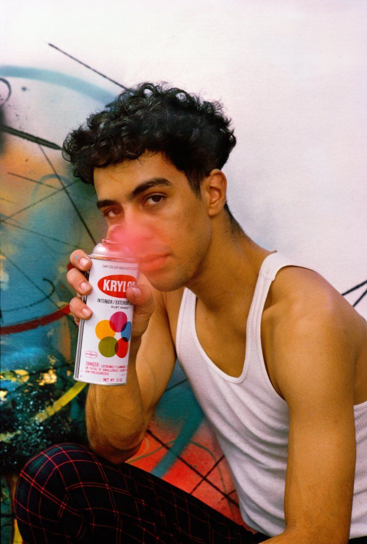 a young man sitting on the ground drinking from a can with his hands in his mouth