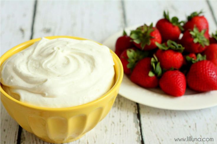 a bowl of whipped cream next to a plate of strawberries