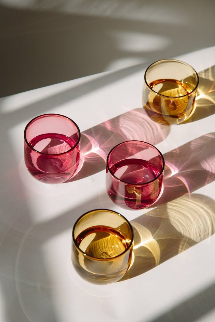 three wine glasses sitting next to each other on a white counter top with shadows coming from them