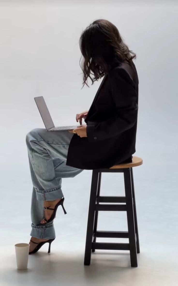 a woman sitting on a stool using a laptop computer