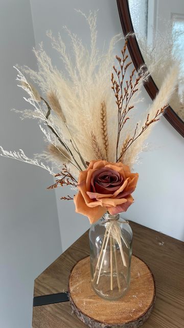 a dried flower in a vase sitting on a wooden stand next to a round mirror