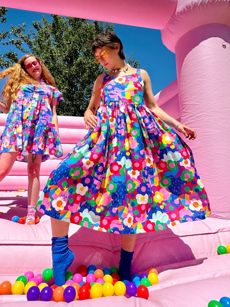 two women in colorful dresses are standing on an inflatable pool with balls and balloons