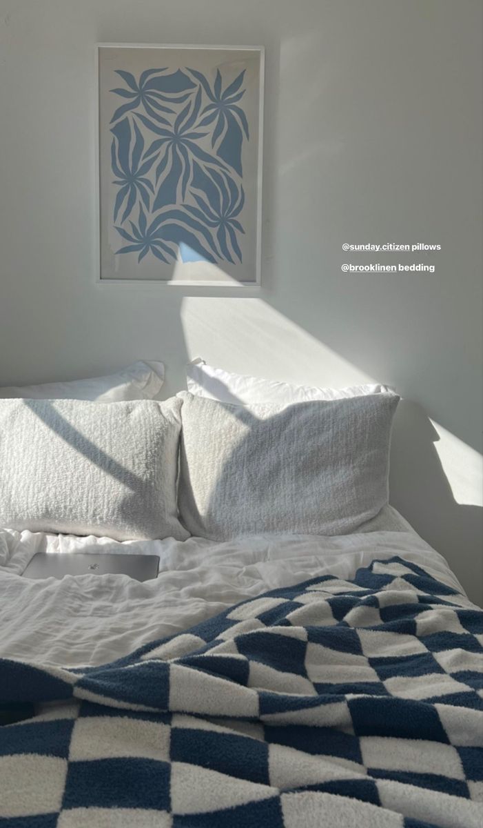 a bed with white and blue comforter in a bedroom next to a painting on the wall