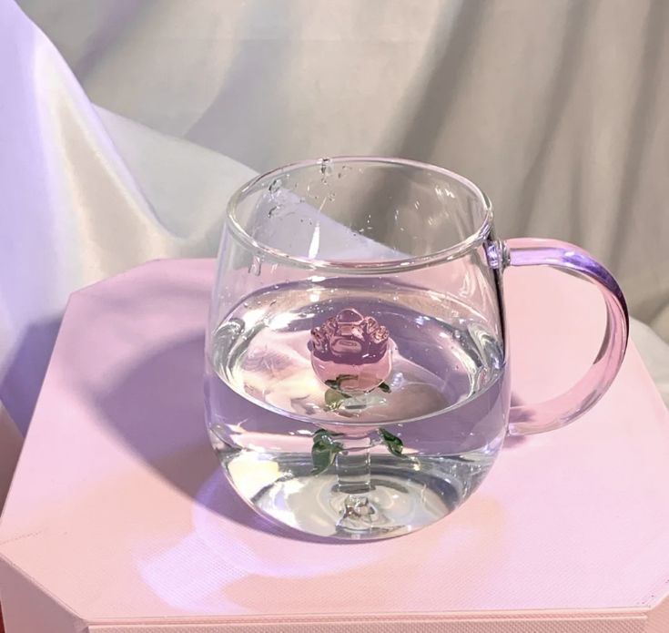 a glass cup with water and flowers in it sitting on top of a pink box