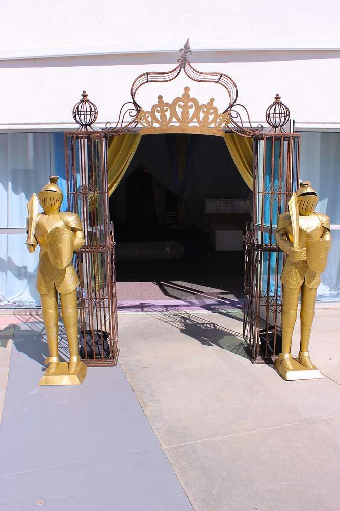 two golden statues are standing in front of an open gate that has a yellow curtain