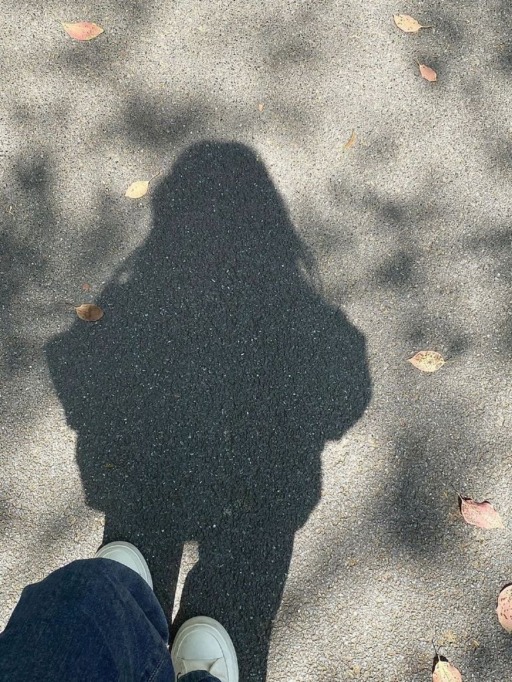 the shadow of a person standing in front of leaves on the ground with their feet up