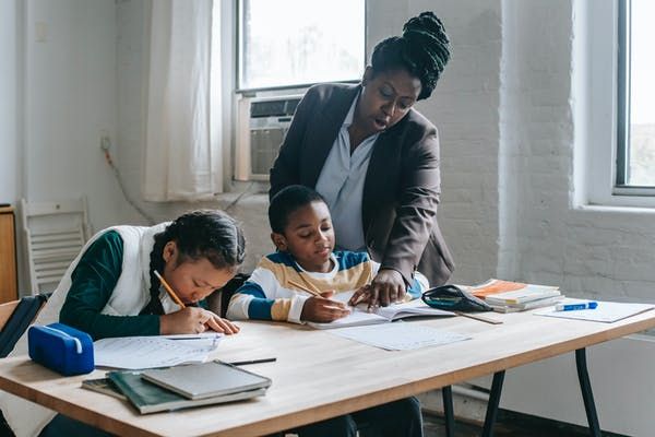 a woman and two children sitting at a table with books on it, writing in notebooks