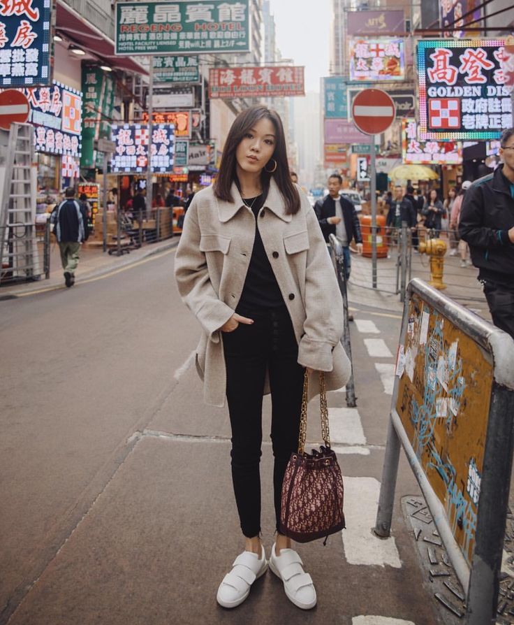 a woman standing on the side of a street holding a handbag in her right hand