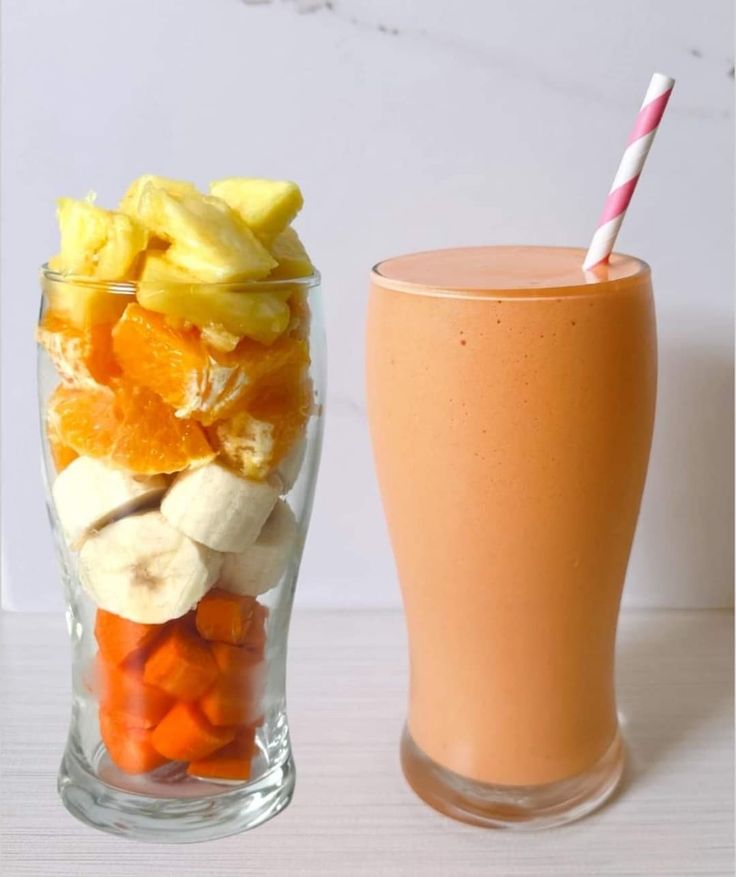 a glass filled with fruit next to a tall cup full of oranges and bananas