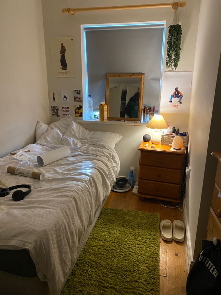 an unmade bed in a small room with a green rug on the floor and a mirror above it