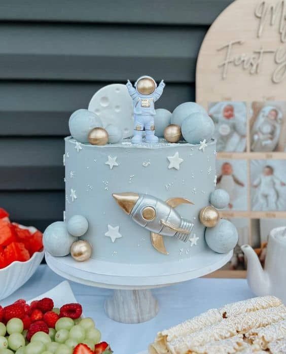 a blue cake with an astronaut on top and other desserts around the edges that include strawberries