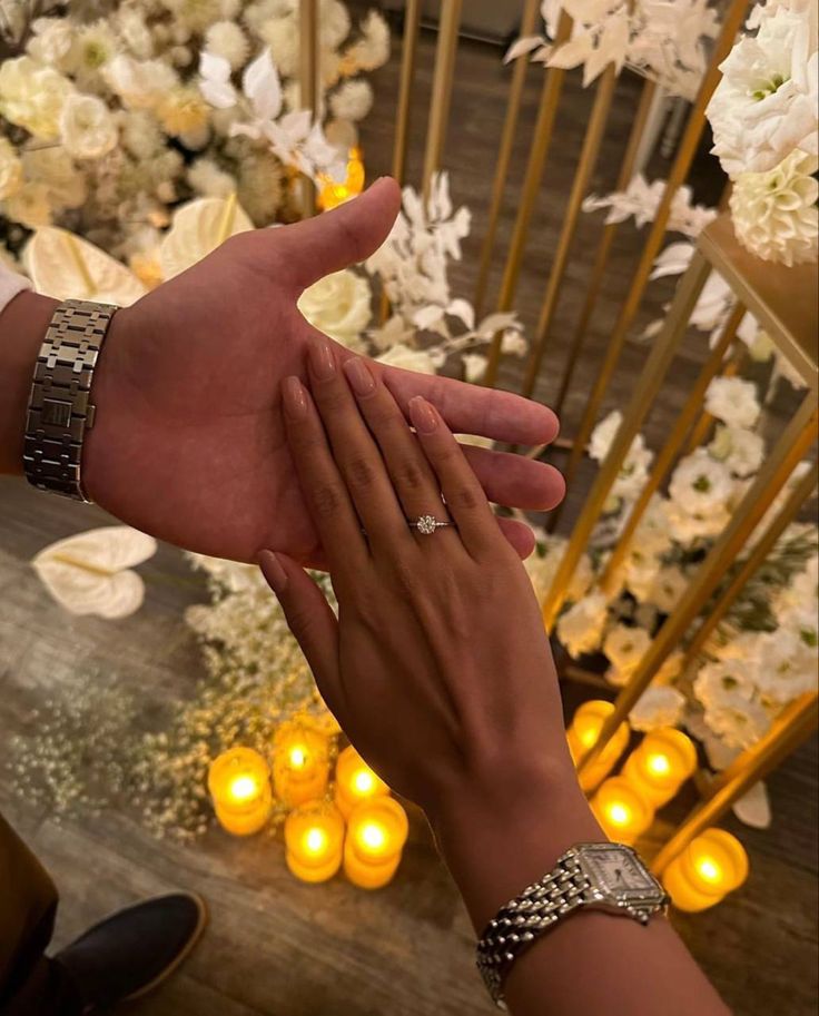 two people holding each other's hand in front of flowers and candles on a table