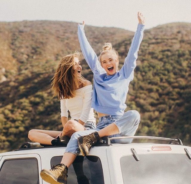 two women sitting on the roof of a car with their arms up in the air