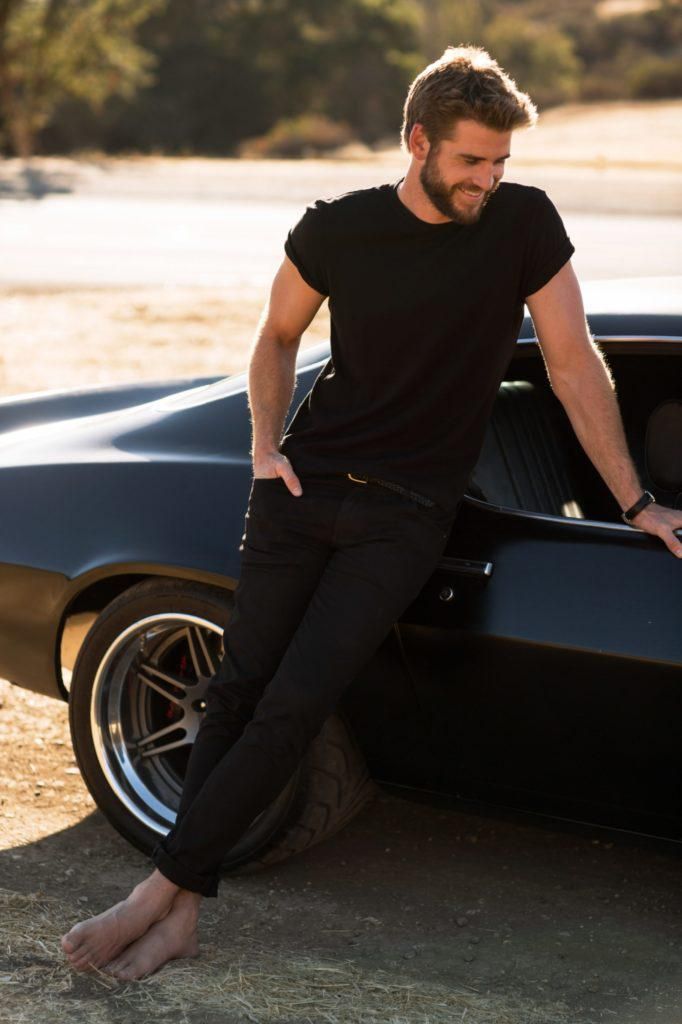 a man leaning on the hood of a black car with his foot propped up against it