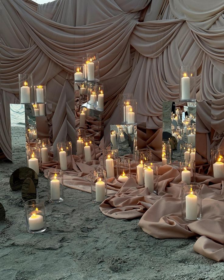 many candles are lit on the ground in front of a wall covered with drapes