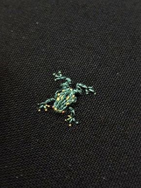 a small green lizard sitting on top of a black cloth covered in tiny beads and thread