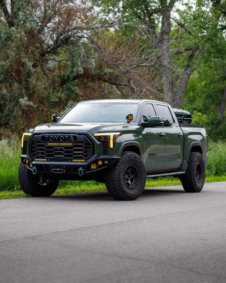 a large green truck parked on the side of a road next to grass and trees