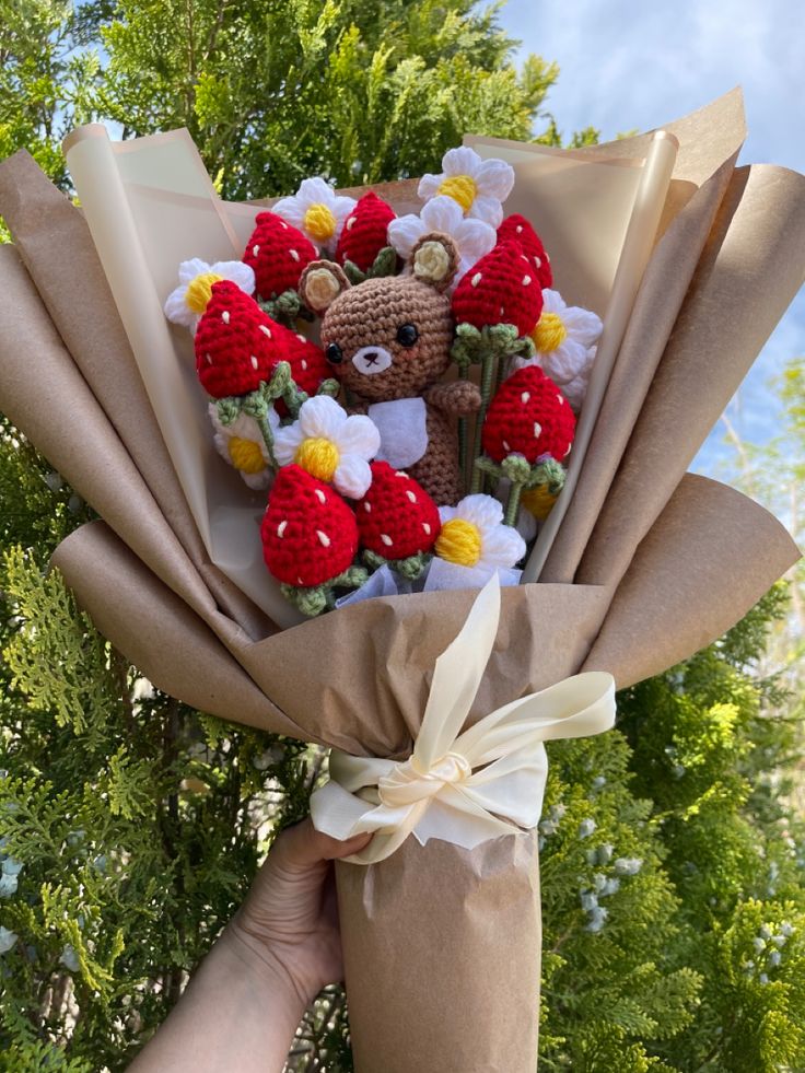 someone is holding a teddy bear wrapped in brown paper with red, yellow and white flowers