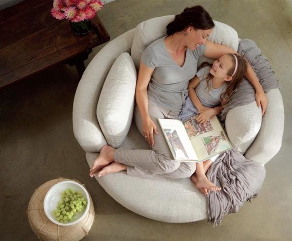 two women and a child are sitting on a round chair with a book in their lap