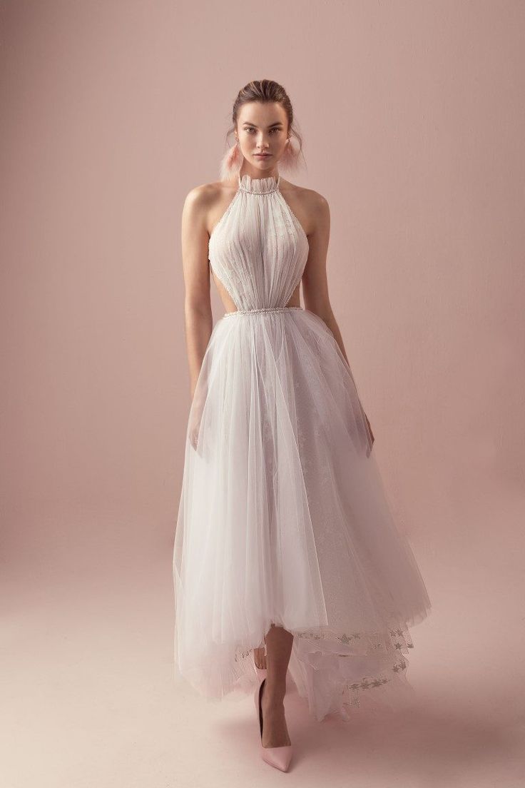 a woman wearing a white dress and high heels standing in front of a pink background