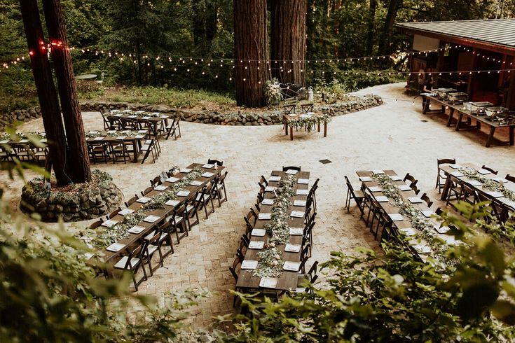 tables and chairs set up in the middle of a forest with string lights strung around them