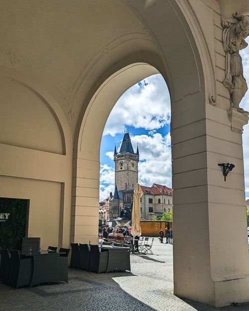 an archway leading to a building with a clock tower in the background and people sitting at tables under it