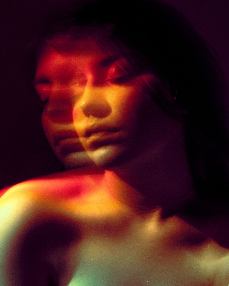 a woman with her arm around her neck and the light shining on her body behind her