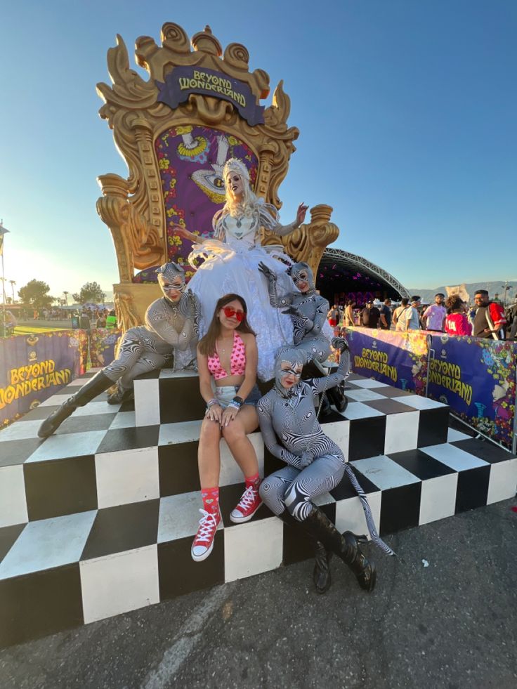 two women sitting on top of a checkered bench in front of a carnival float