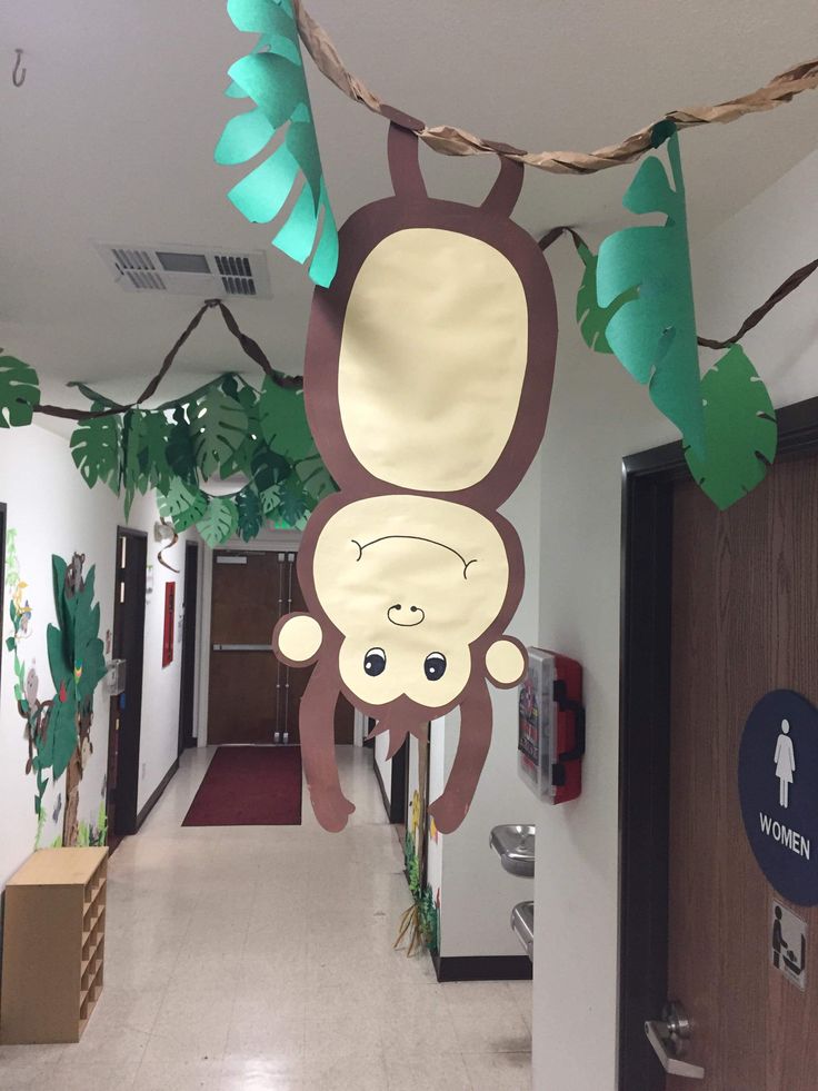 a monkey hanging from the ceiling next to a door in a hallway with green leaves