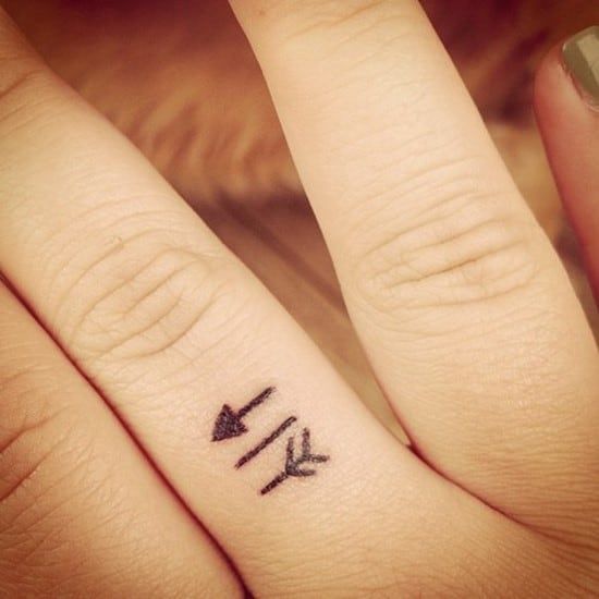 two fingers with small tattoos on them, one has an arrow and the other has arrows